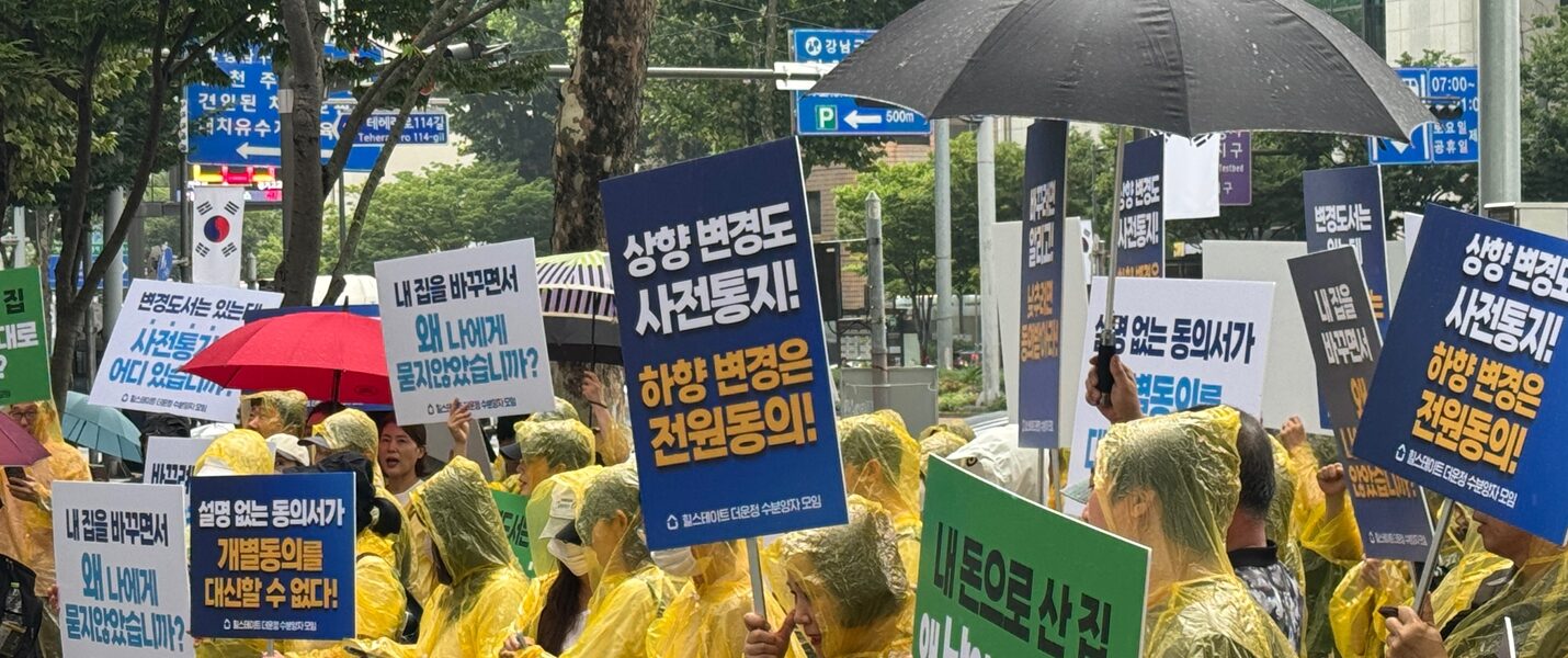 22일 서울 강남경찰서 인근에서 열린 집회에서 우비를 입은 '힐스테이트 더 운정' 수분양자들이 비를 맞으며 '상향 변경도 사전통지, 하향 변경은 전원동의', '설명 없는 동의서가 개별동의를 대신할 수 없다', '내 돈으로 산 집, 왜 남이 마음대로 바꿉니까' 등이 적힌 피켓을 들고 있다.