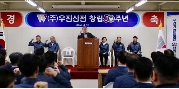 김영창 우진산전 회장이 2024년 4월 10일 열린 창립 50주년 기념식에서 연단에 올라 직원들과 함께 주먹을 들어 보이고 있다. (출처=우진산전)